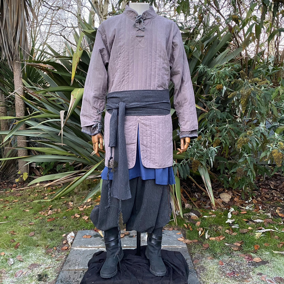 Medieval LARP outfit front view with grey gambeson, waist sash, greenery backdrop.