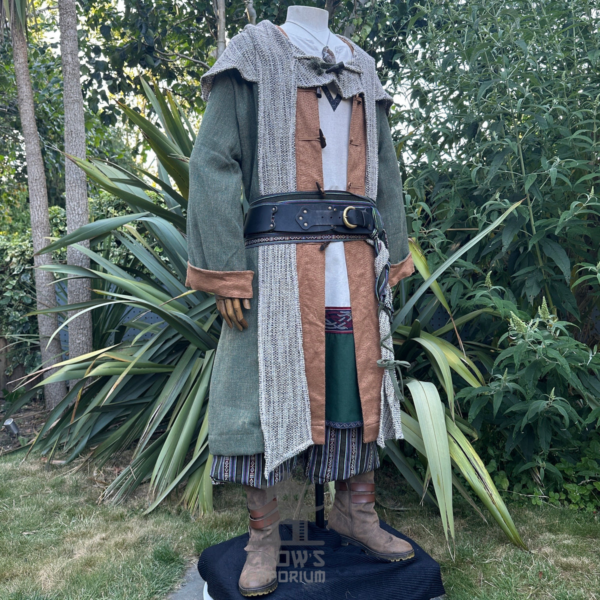 Medieval LARP coat front view, ornate belt and boots, leafy backdrop.