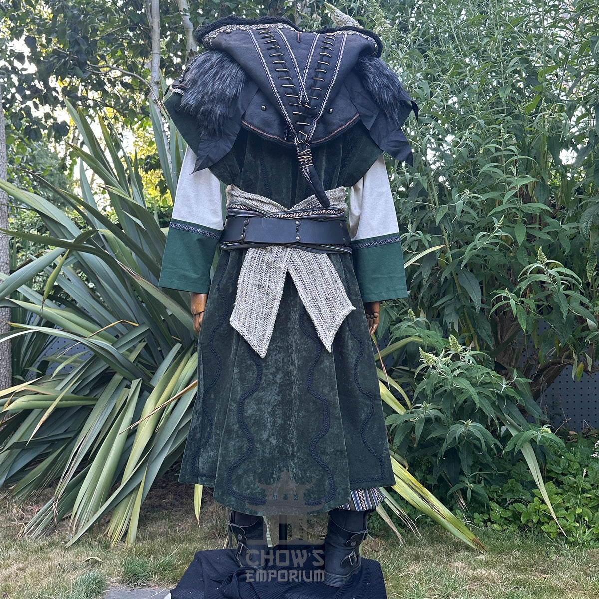 Medieval LARP costume back view featuring a long green waistcoat, black faux leather hood and vambraces. For Renaissance Faire and historical roleplay events.