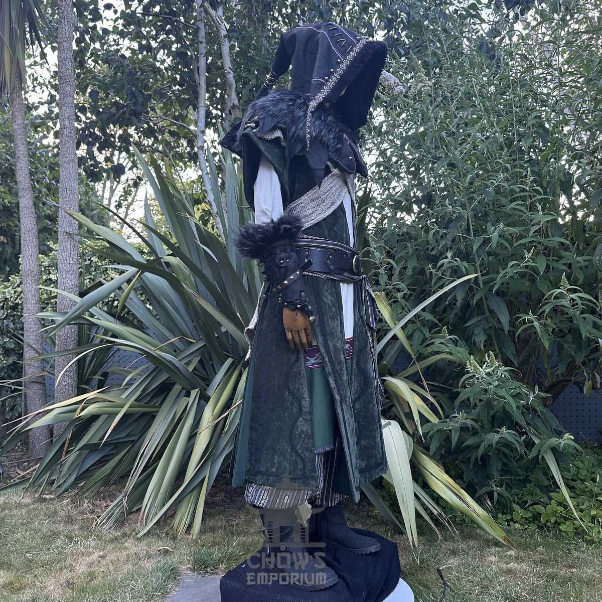 Medieval LARP costume side view featuring a long green waistcoat, black faux leather hood and vambraces. For Renaissance Faire and historical roleplay events.