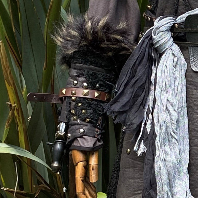 Black fur-trimmed medieval vambraces with studs on a mannequin arm, side view.