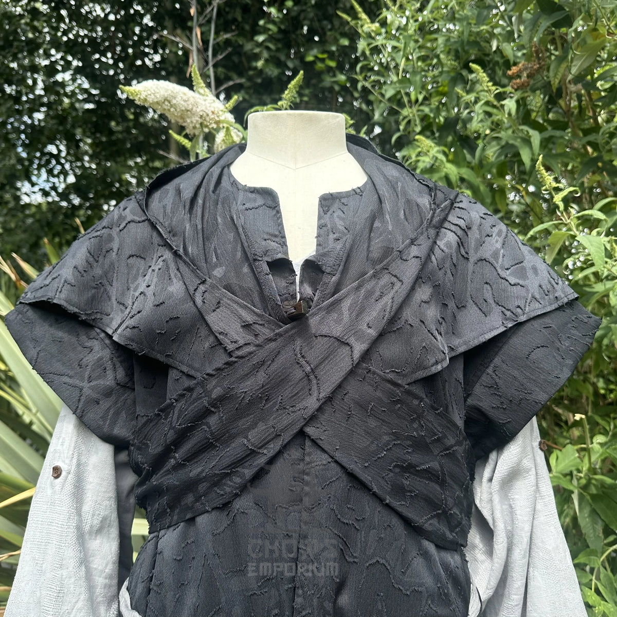 Close detail of the black hood crossed over the chest above the distressed panelling of the waistcoat.