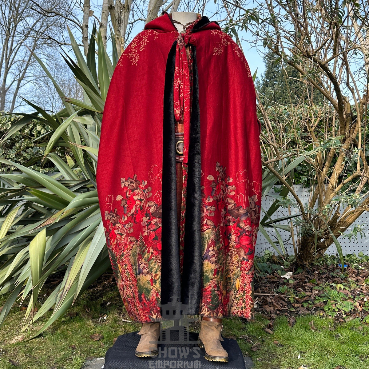 Crimson cloak on mannequin, floral embroidery, outdoor setting.