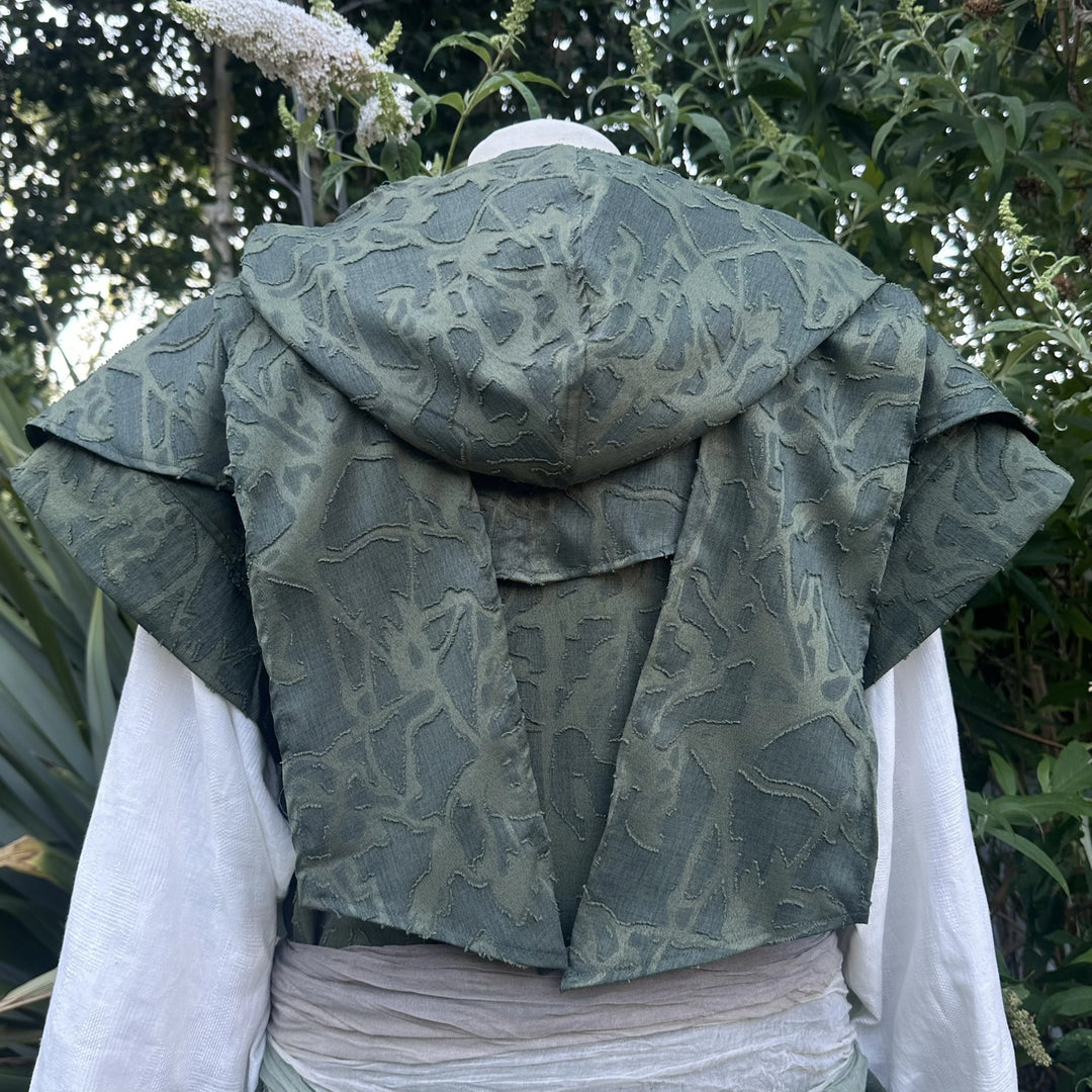 Green panelled waistcoat and hood set, hood up with the ends draped as a cape across the shoulders, back view. Belt sold separately.