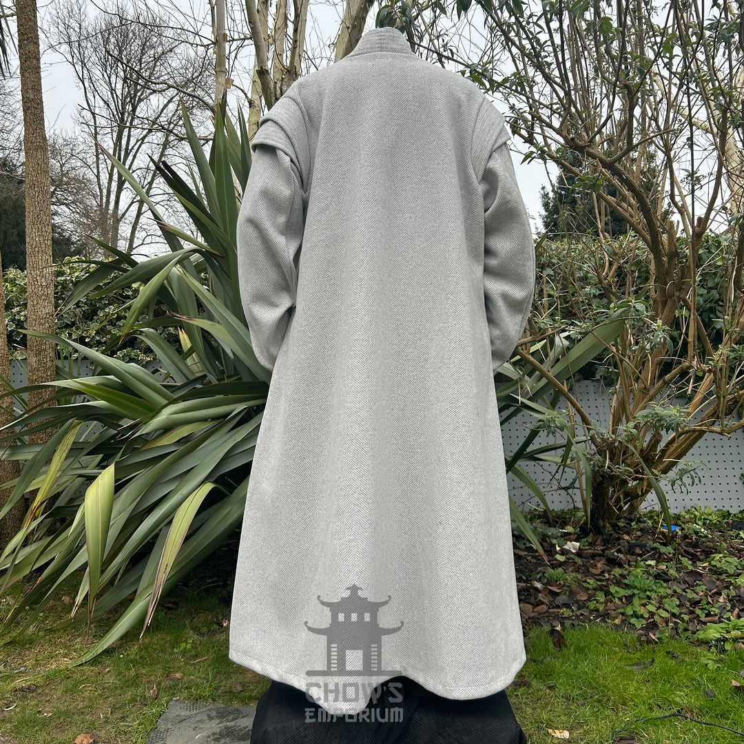 A light grey full-length robe displayed on a mannequin, shown from back view, featuring a herringbone pattern, in a garden setting.
