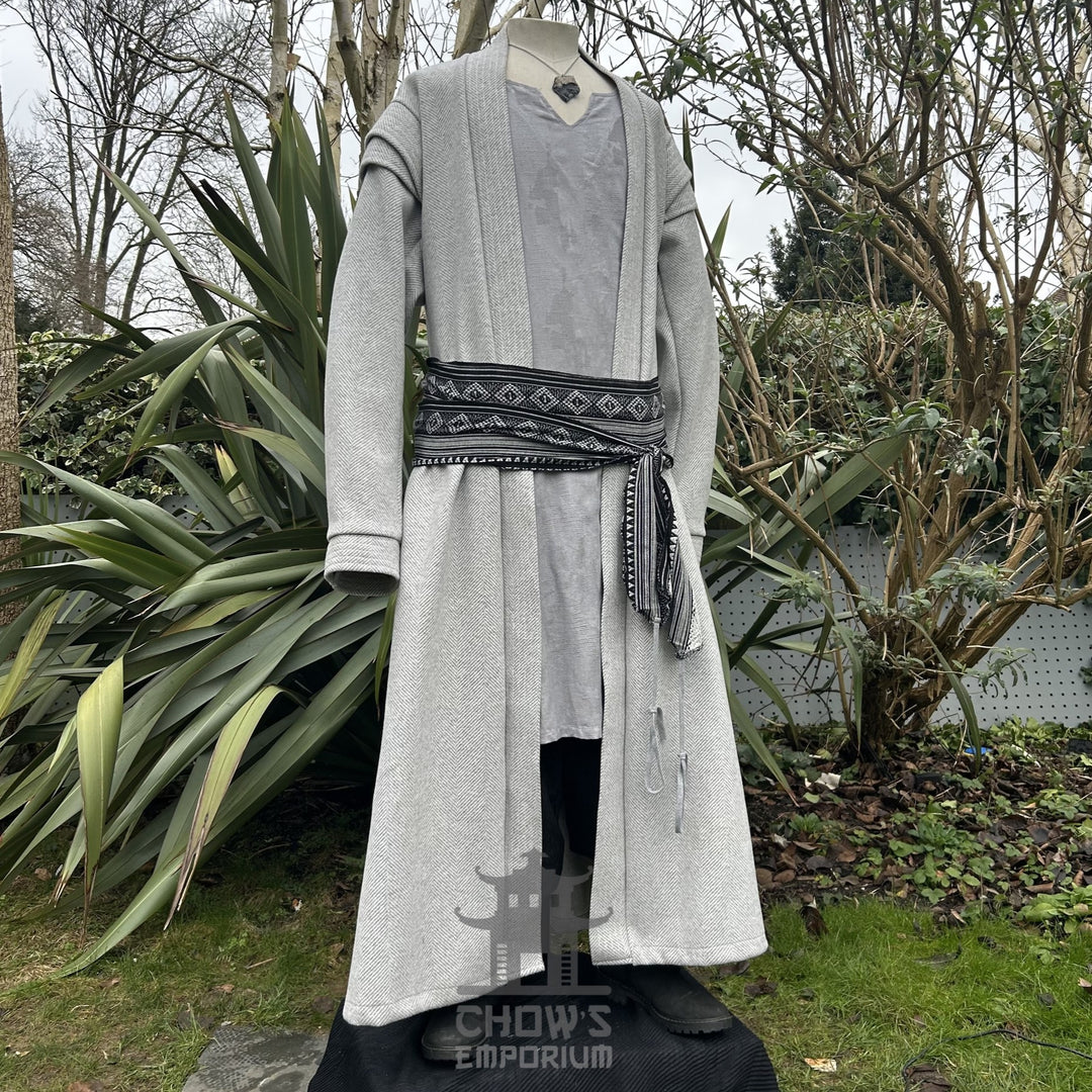 A light grey full-length robe displayed open with sash belt on a mannequin, shown from side view, featuring a herringbone pattern, in a garden setting.