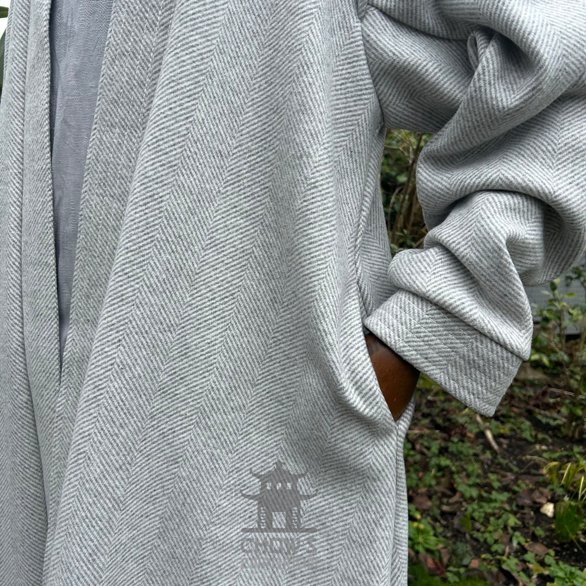 Sleeve and pocket detail on light grey herringbone robe with outdoor background.