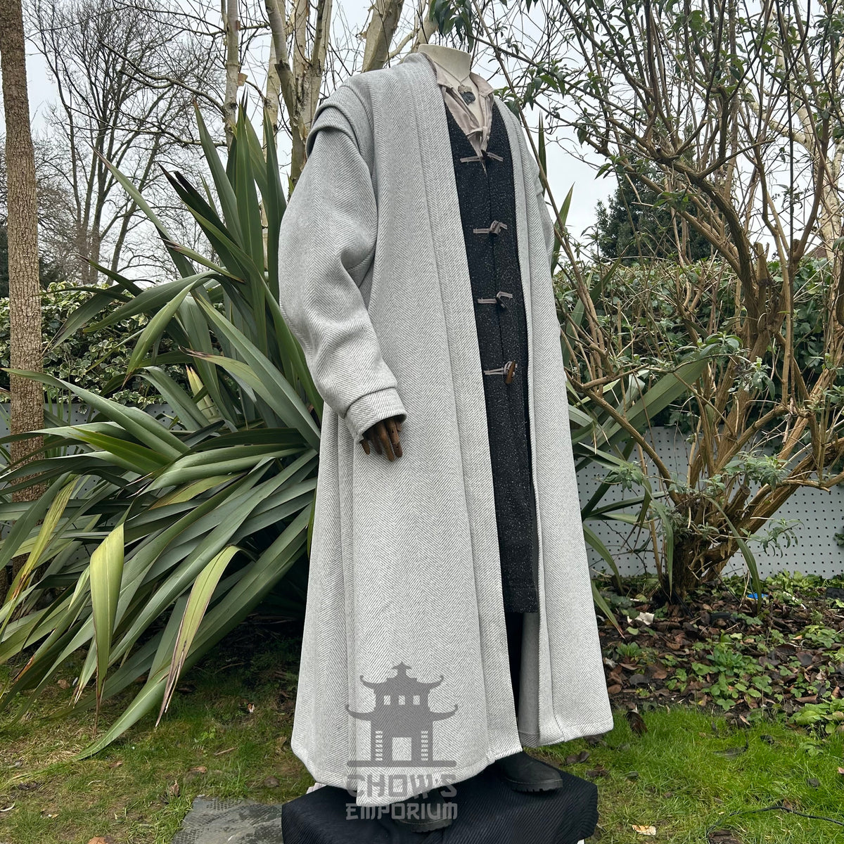 A light grey full-length robe displayed on a mannequin, shown from side view, featuring a herringbone pattern, in a garden setting.