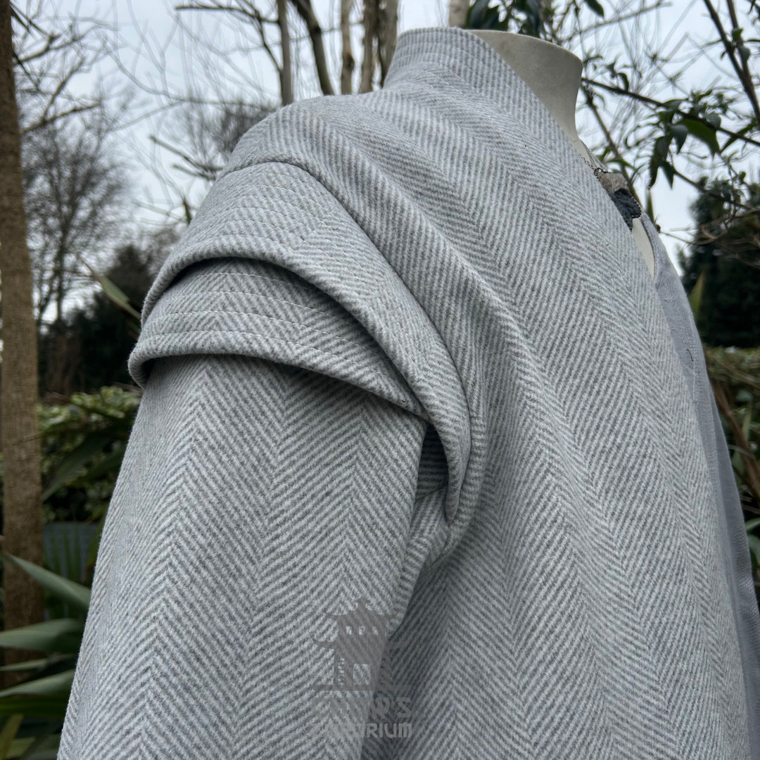 A light grey robe shoulder sleeve detail displayed on a mannequin, shown from side view, featuring a herringbone pattern, with a garden background.