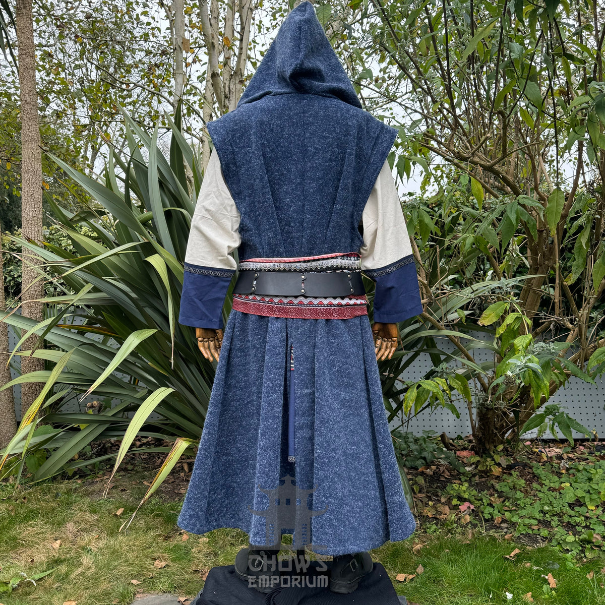 Mannequin wearing a blue hooded sleeveless robe with a patterned belt shown from back view in an outdoor setting.