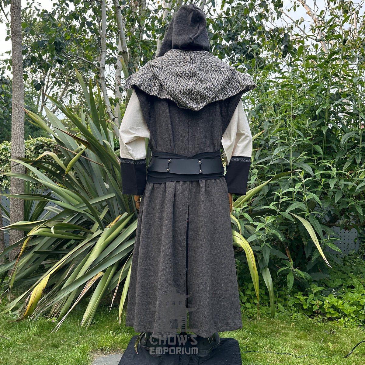 Back view of mannequin wearing hooded brown herringbone sleeveless robe with scarf hood, in garden setting.