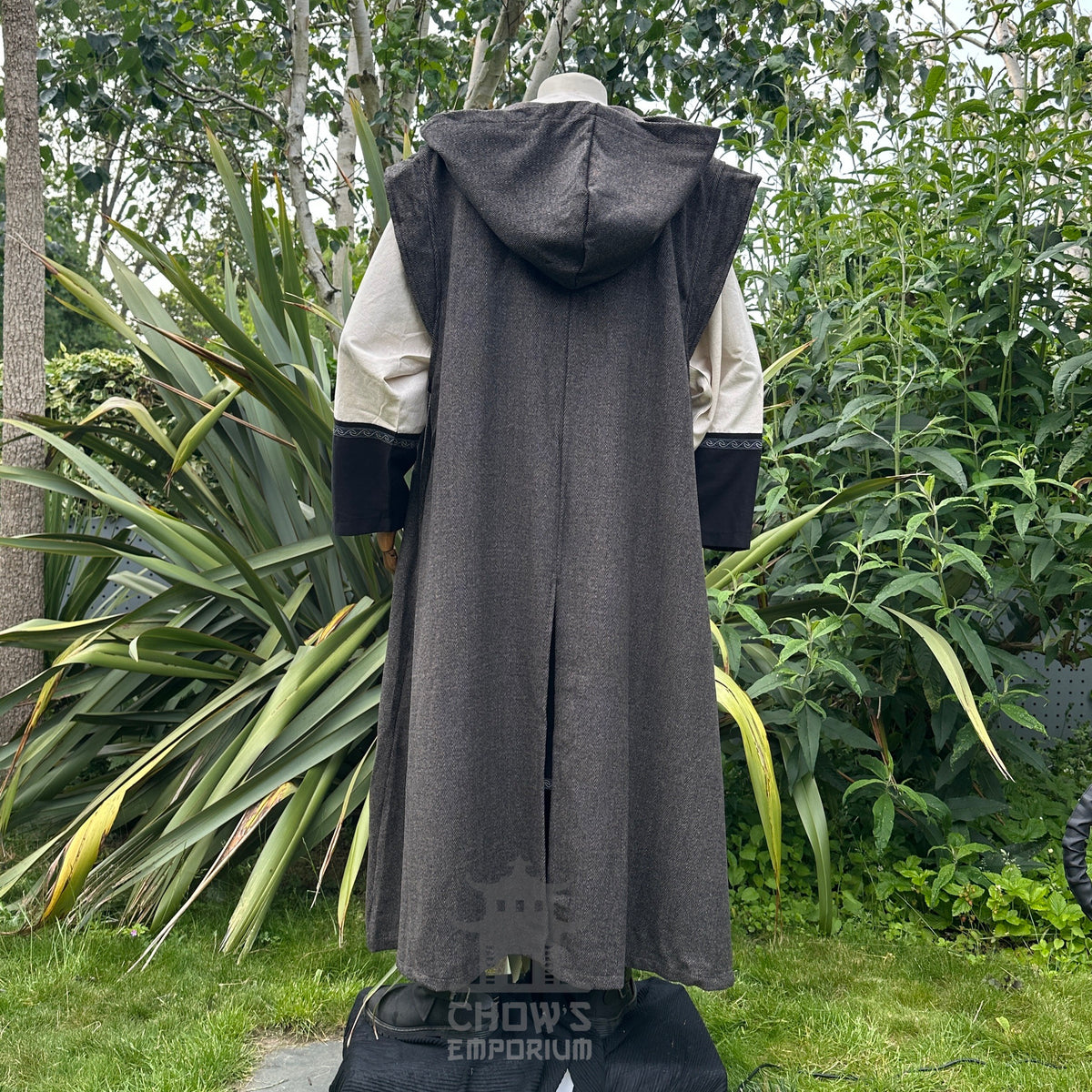 Back view of mannequin in full length, hooded brown herringbone sleeveless robe, in garden setting..