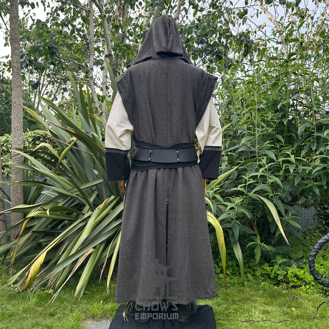 Back view of mannequin wearing hooded brown herringbone sleeveless robe with black belt, in garden setting.