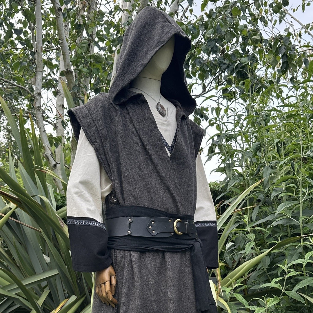 Cropped side view of mannequin in hooded brown herringbone sleeveless robe with black belt, in garden setting.