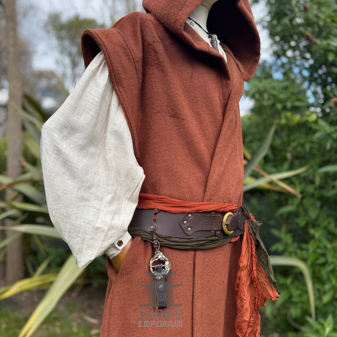 Person wearing a rust hooded robe with a key pendant in an outdoor setting