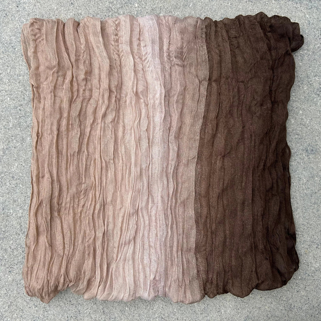 A square scarf with a horizontal ombre gradient transitioning from light taupe at the top to medium beige and dark brown at the bottom, laid flat on a gray textured surface.