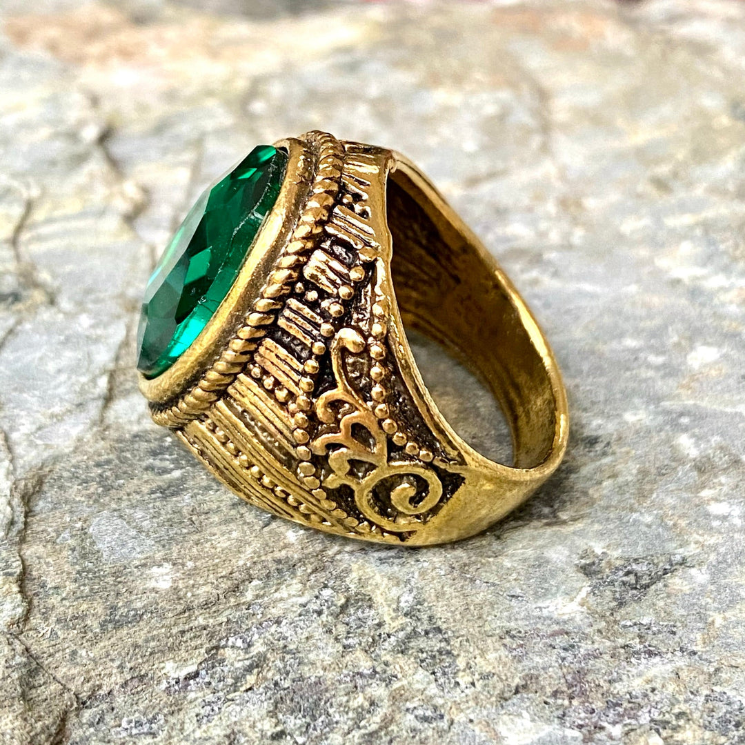 Ornate medieval gold ring with green gemstone on textured surface.