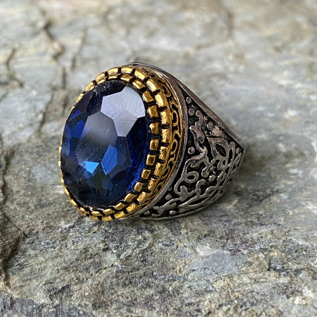 Ornate medieval ring with dark blue gem on textured stone surface.
