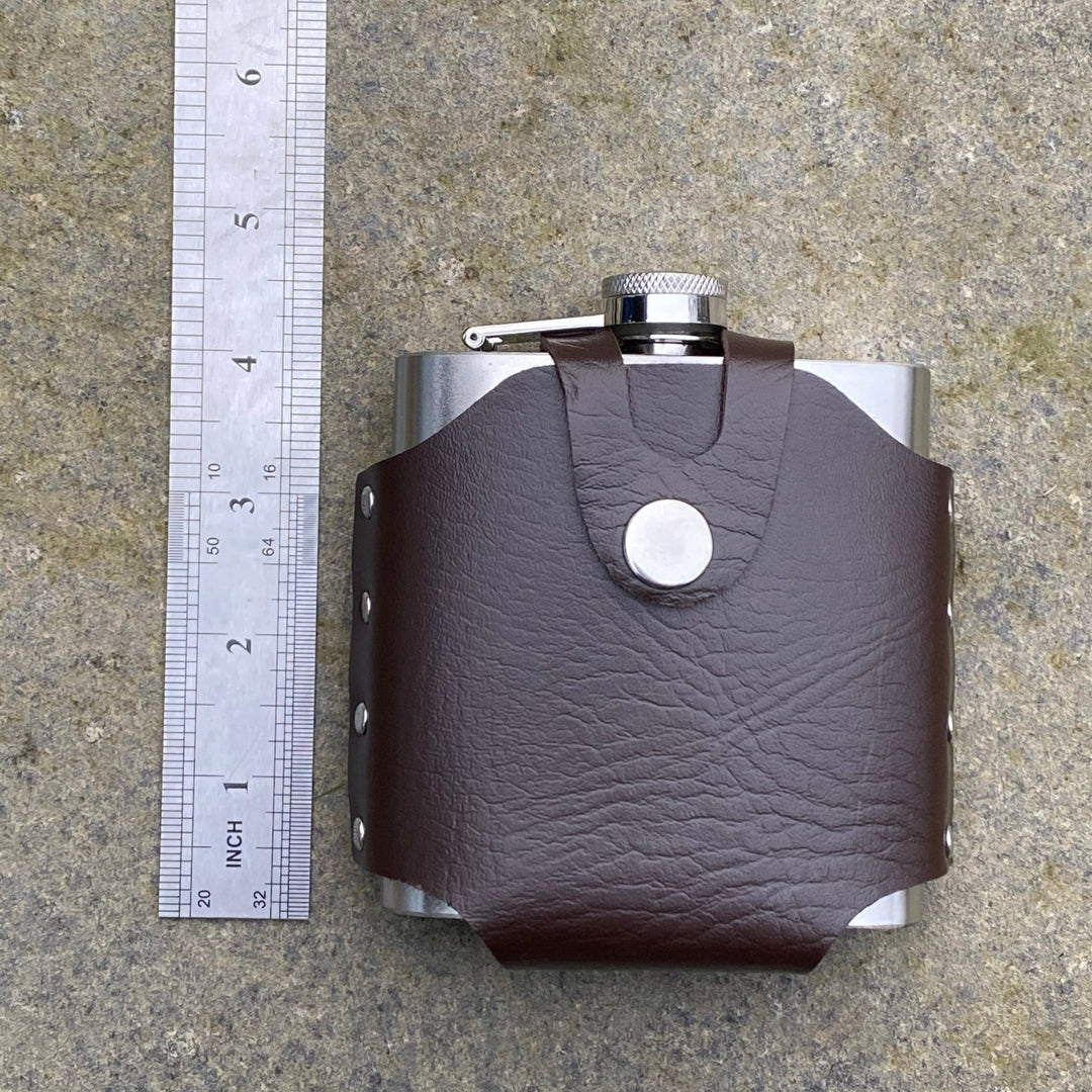 Brown leather-bound flask with belt holder, ruler for size, on stone surface. LARP accessory.