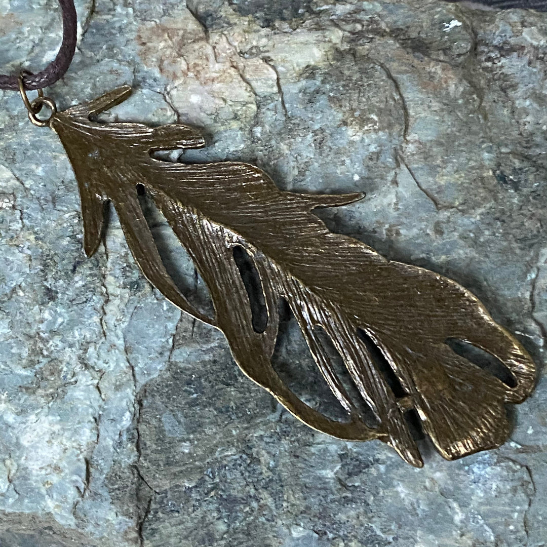 Brass feather necklace on stone, detailed texture, LARP medieval accessory.