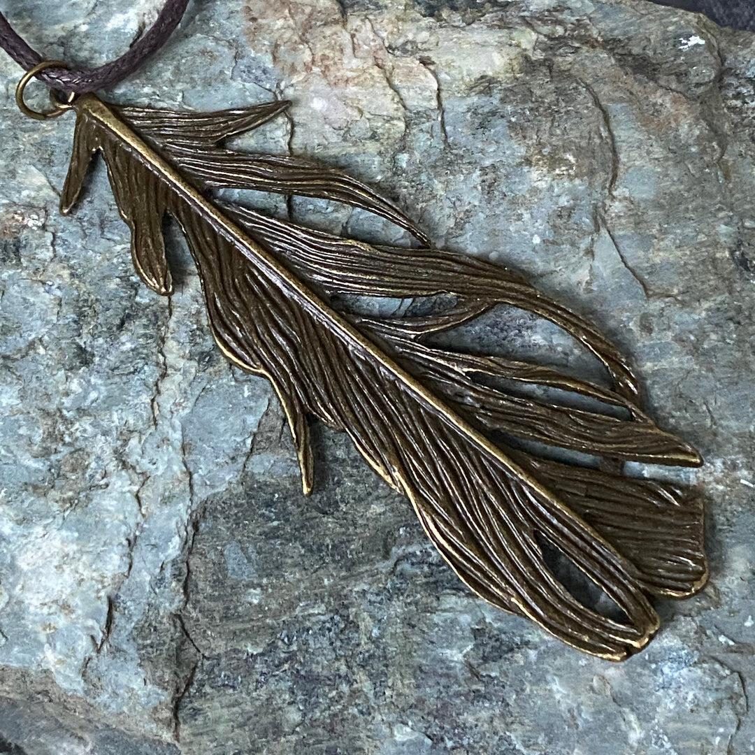 Brass feather amulet necklace on rock surface for LARP.