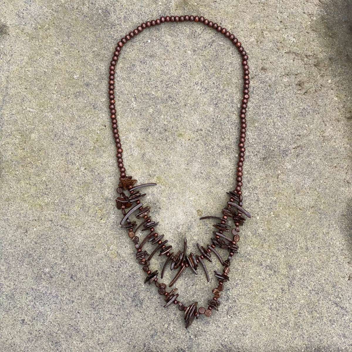 Brown LARP necklace with tooth design on stone backdrop.