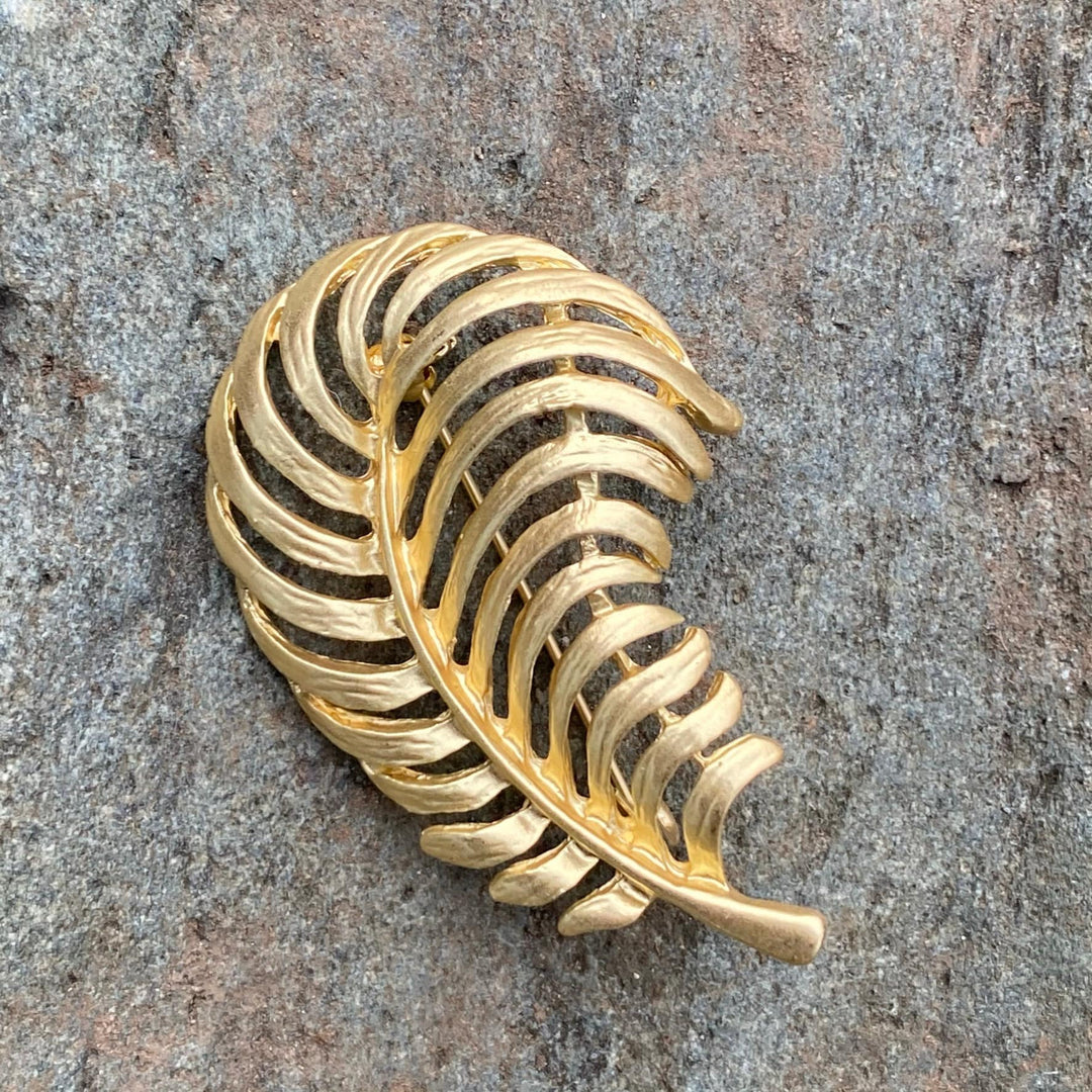 Golden fern-shaped brooch on stone backdrop for medieval LARP attire.