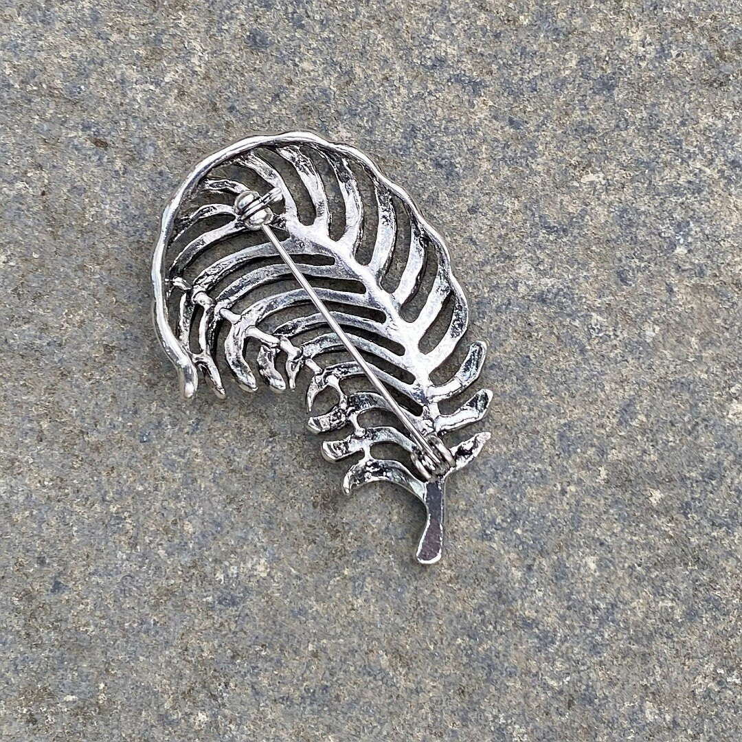Medieval LARP silver fern brooch back view on stone surface.