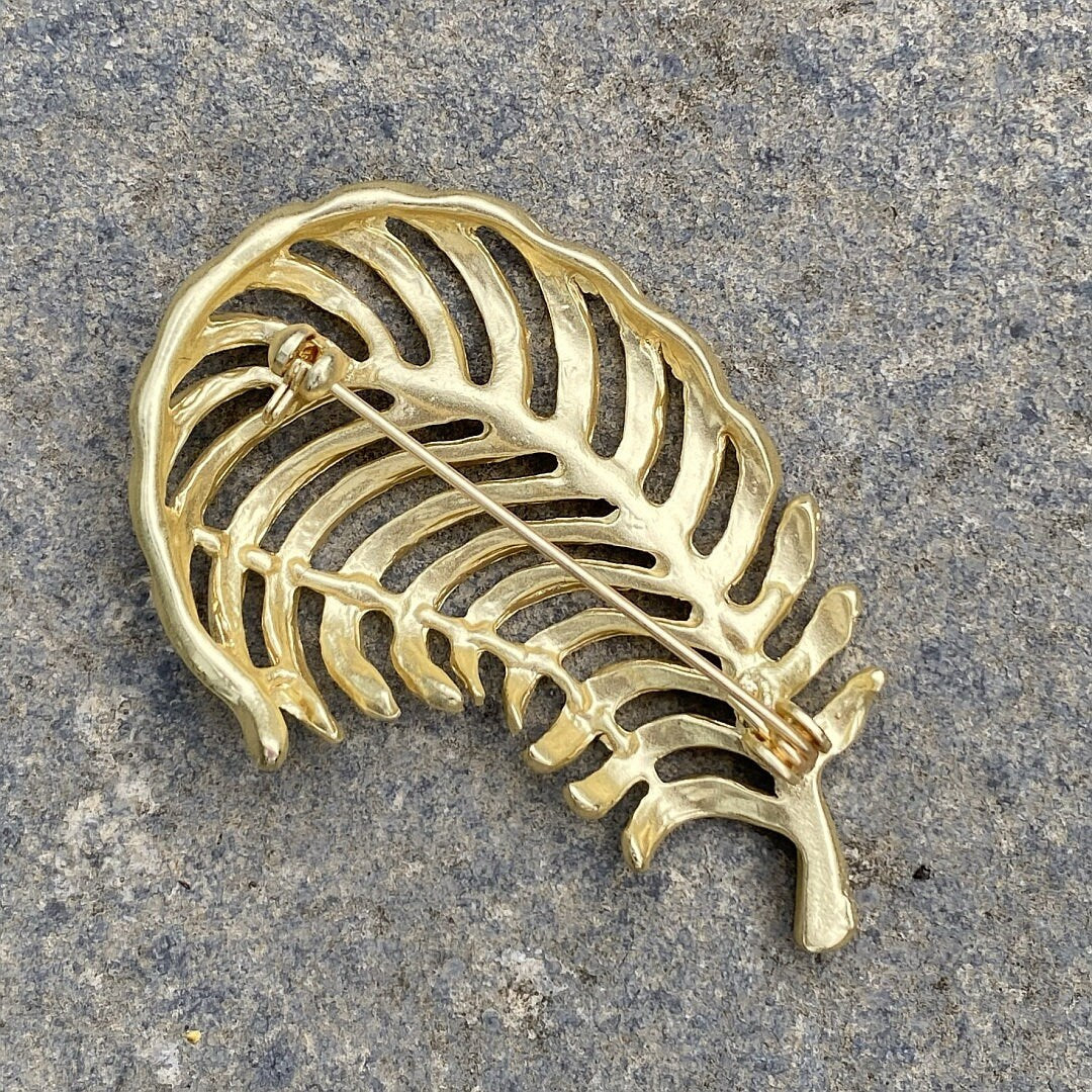 Gold fern brooch with openwork design, seen from back on stone surface, LARP style.