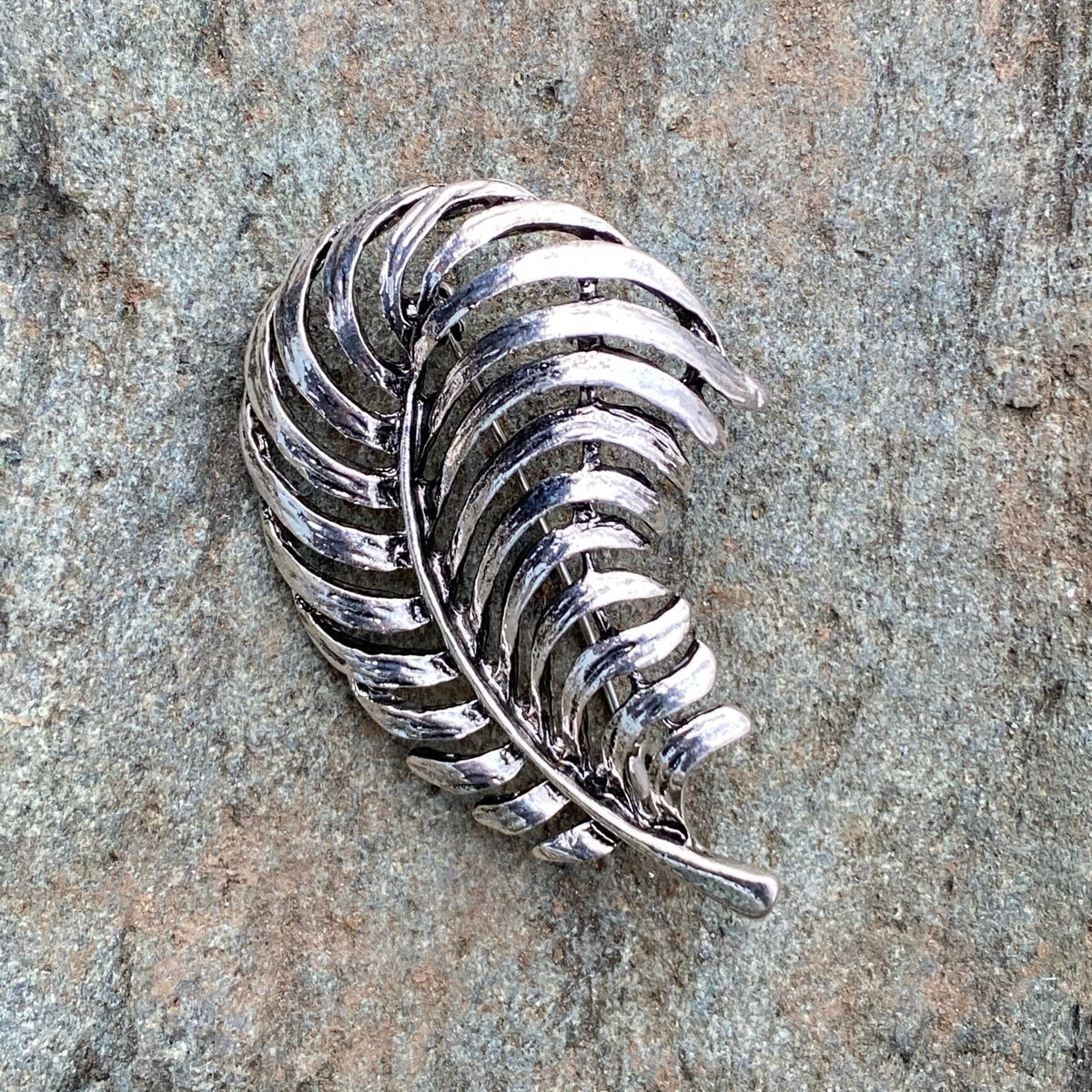 Silver fern-shaped LARP pin on textured stone background, medieval style.