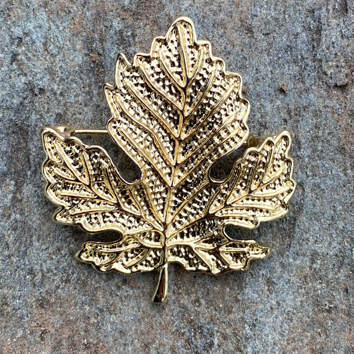 Elven gold leaf brooch with intricate detail on a textured stone background.