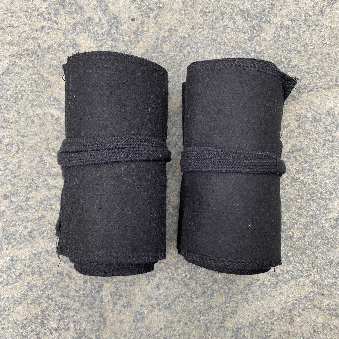 Two rolled black wool leg wraps on stone for medieval LARP.