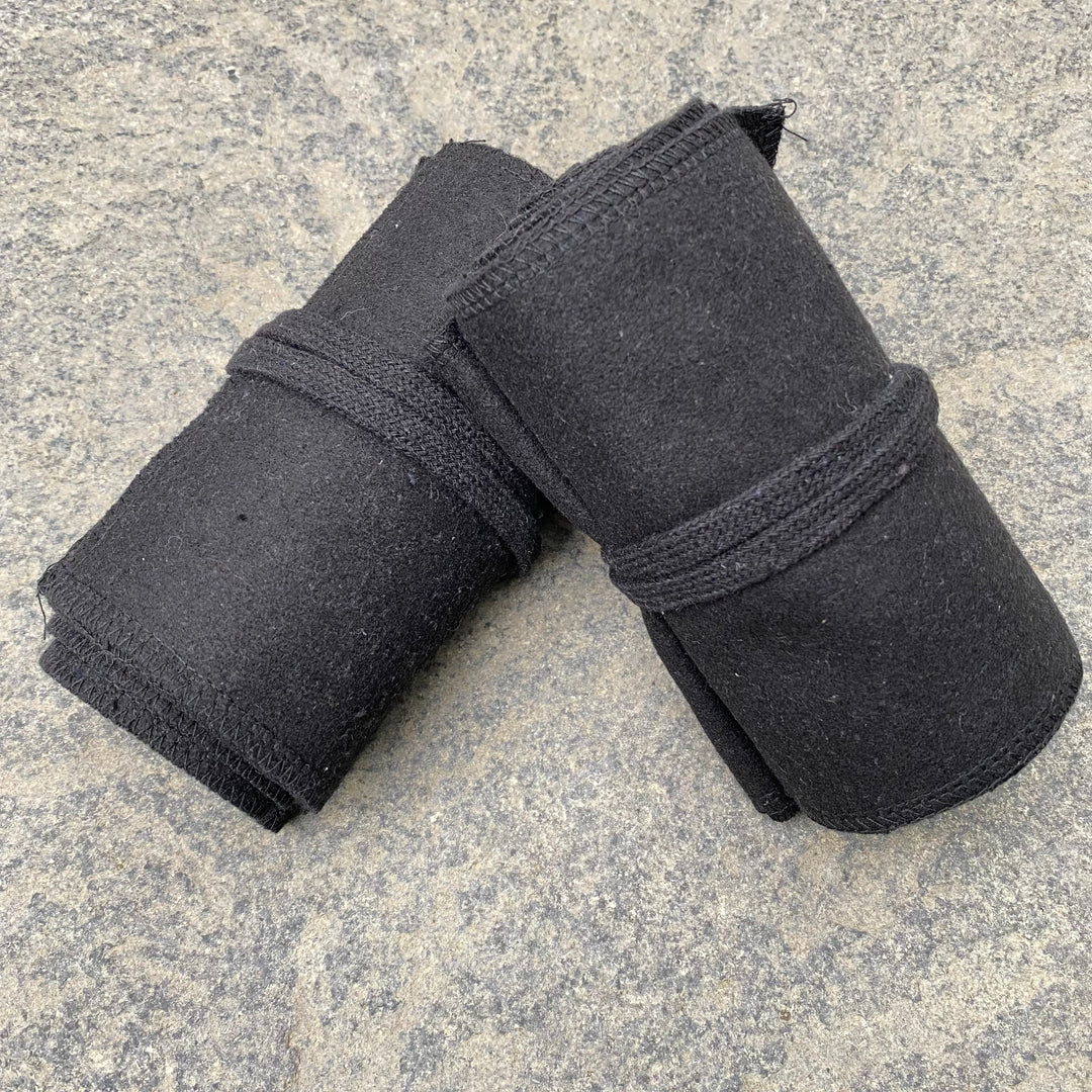 Black wool LARP leg wraps rolled on stone surface, close-up view.