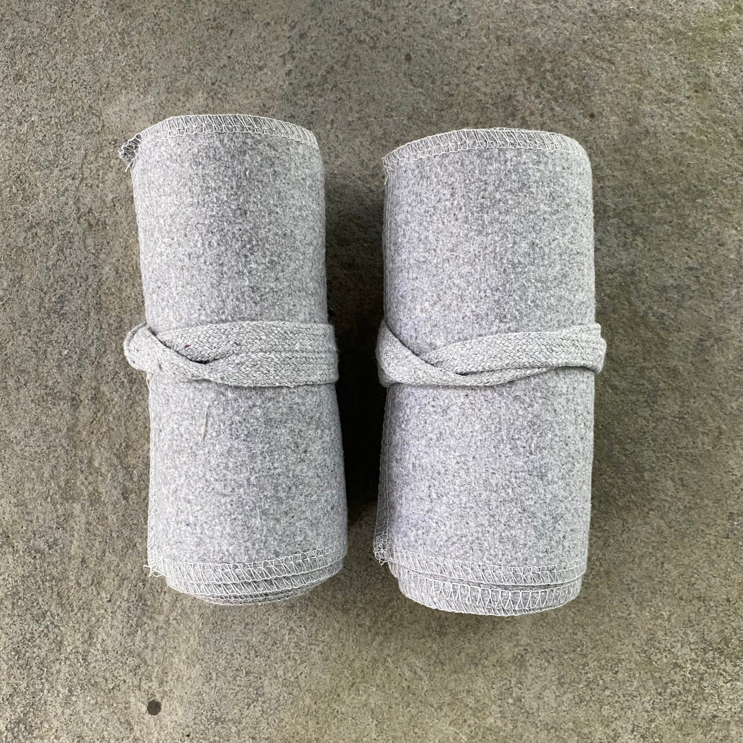 Two rolled light grey wool leg wraps for medieval LARP on stone surface.