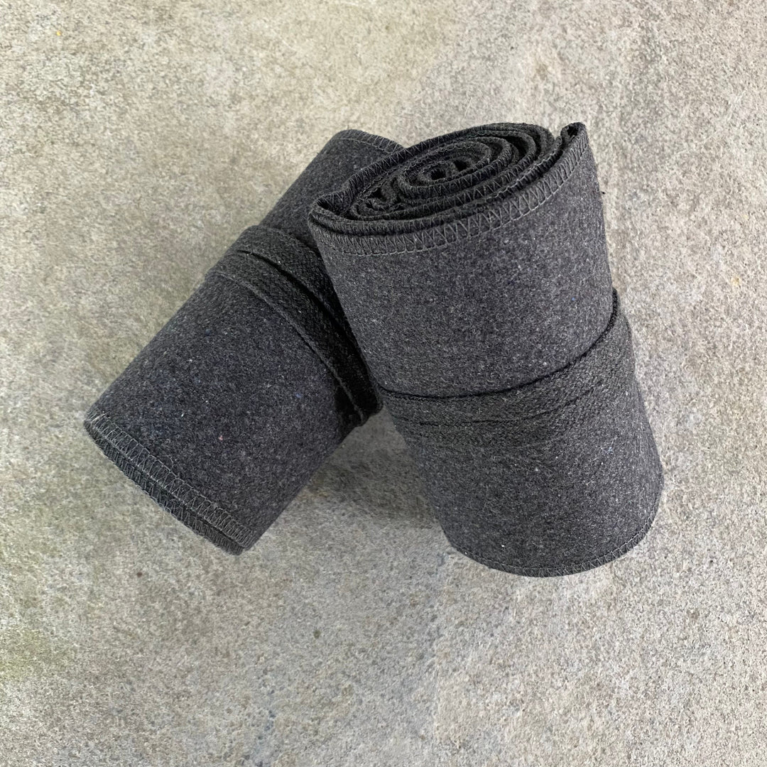 Dark grey wool leg wraps for LARP, rolled on stone surface.