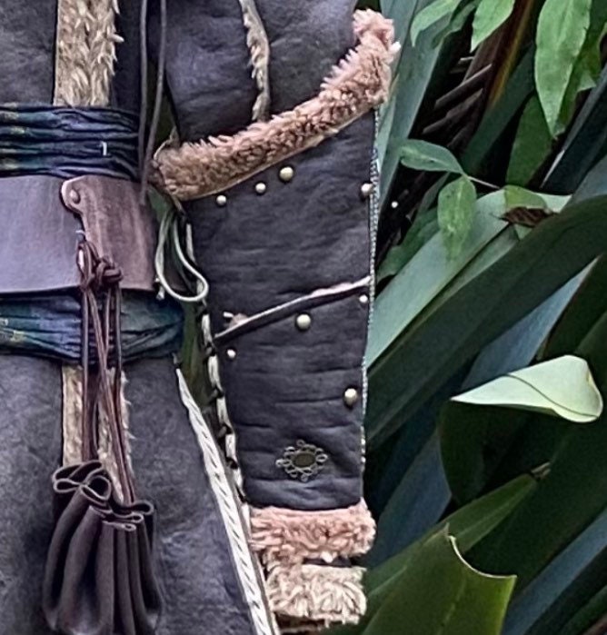 Green medieval LARP vambrace close-up with fur trim and rivet details.