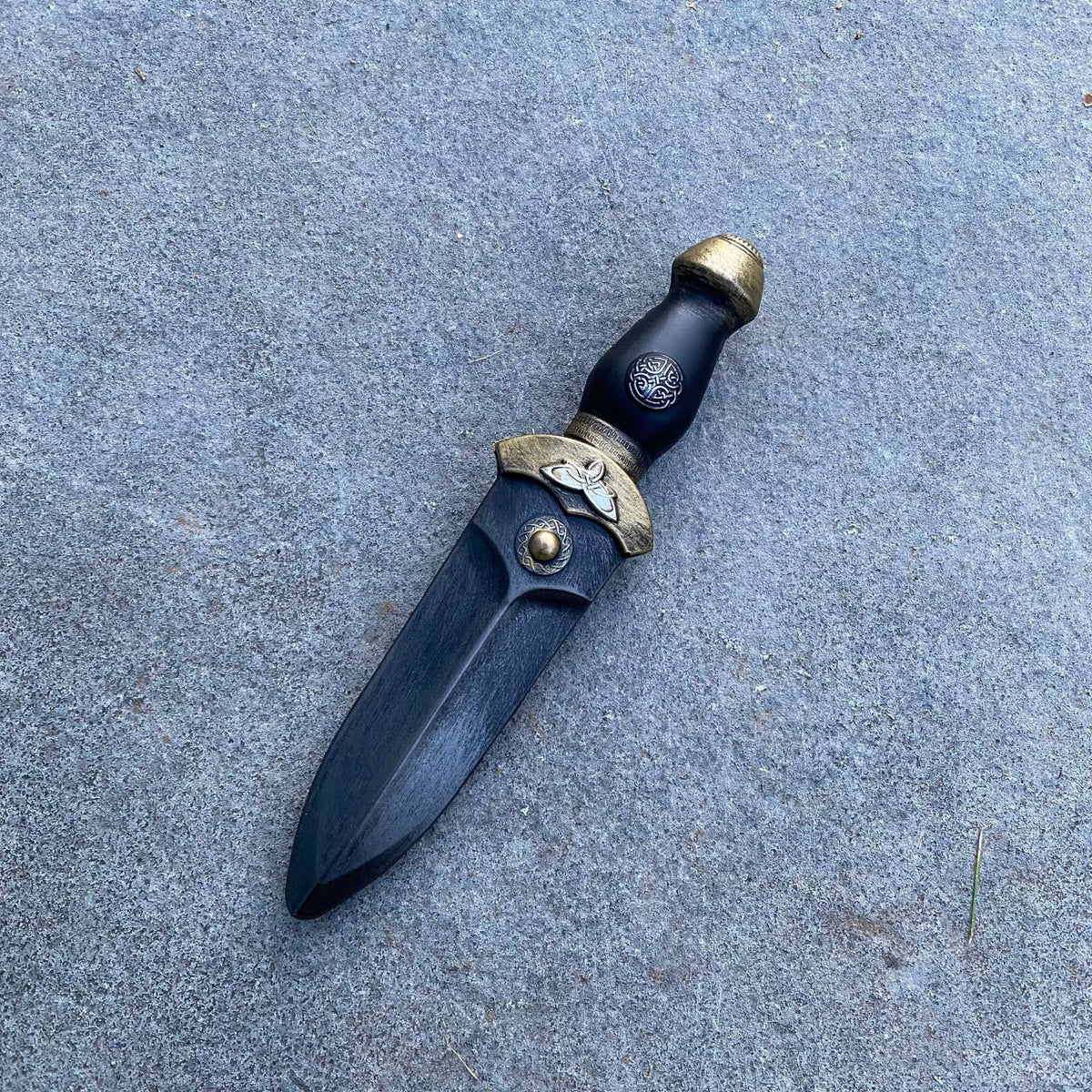 Medieval LARP dagger close-up, ornate gold details on handle, stone background.