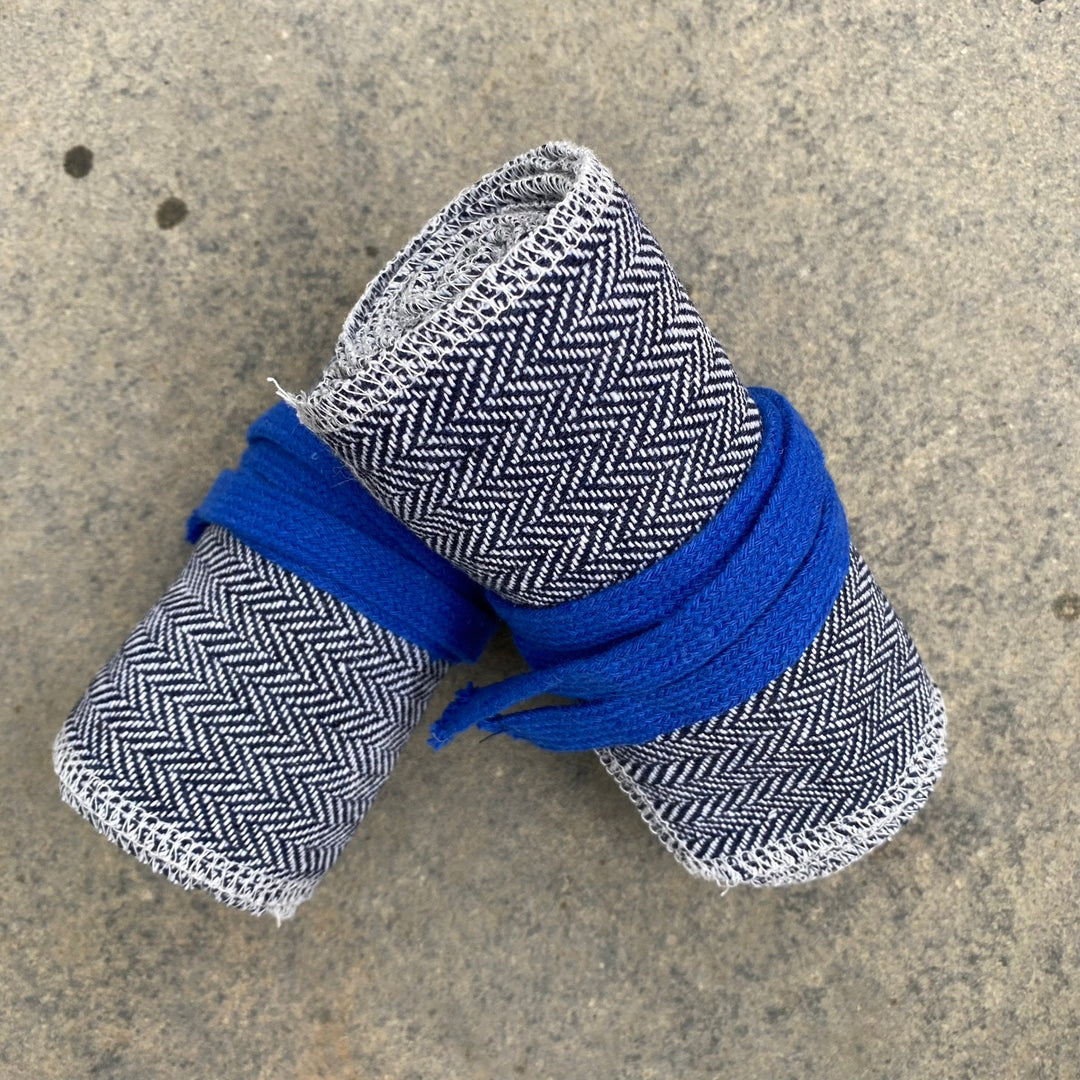 Medieval LARP leg wraps in herringbone wool, rolled with blue ties on stone.