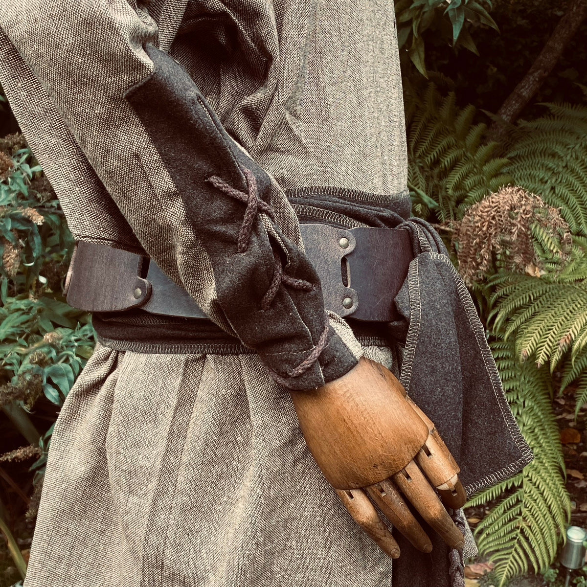 Wooden mannequin in medieval wool shirt, side view with rugged belt.