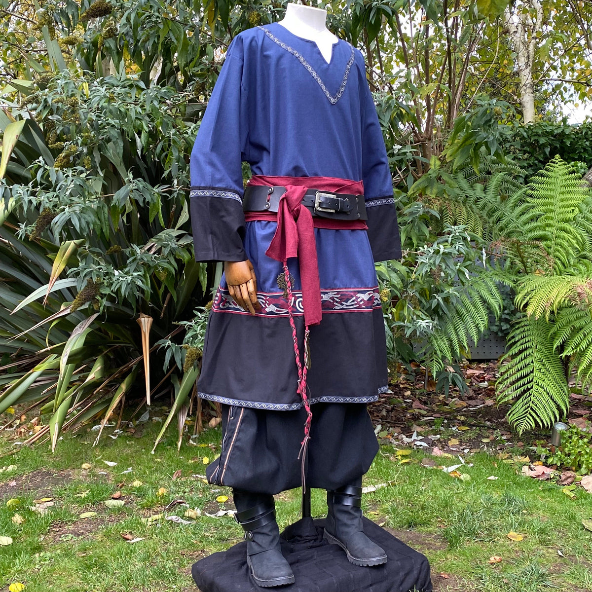 Medieval LARP outfit side view, featuring a blue and black Viking tunic, trousers and sash.