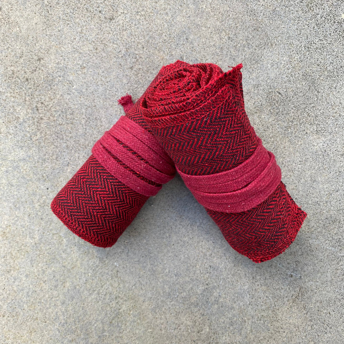 Red herringbone wool leg wraps rolled for medieval LARP, top view.