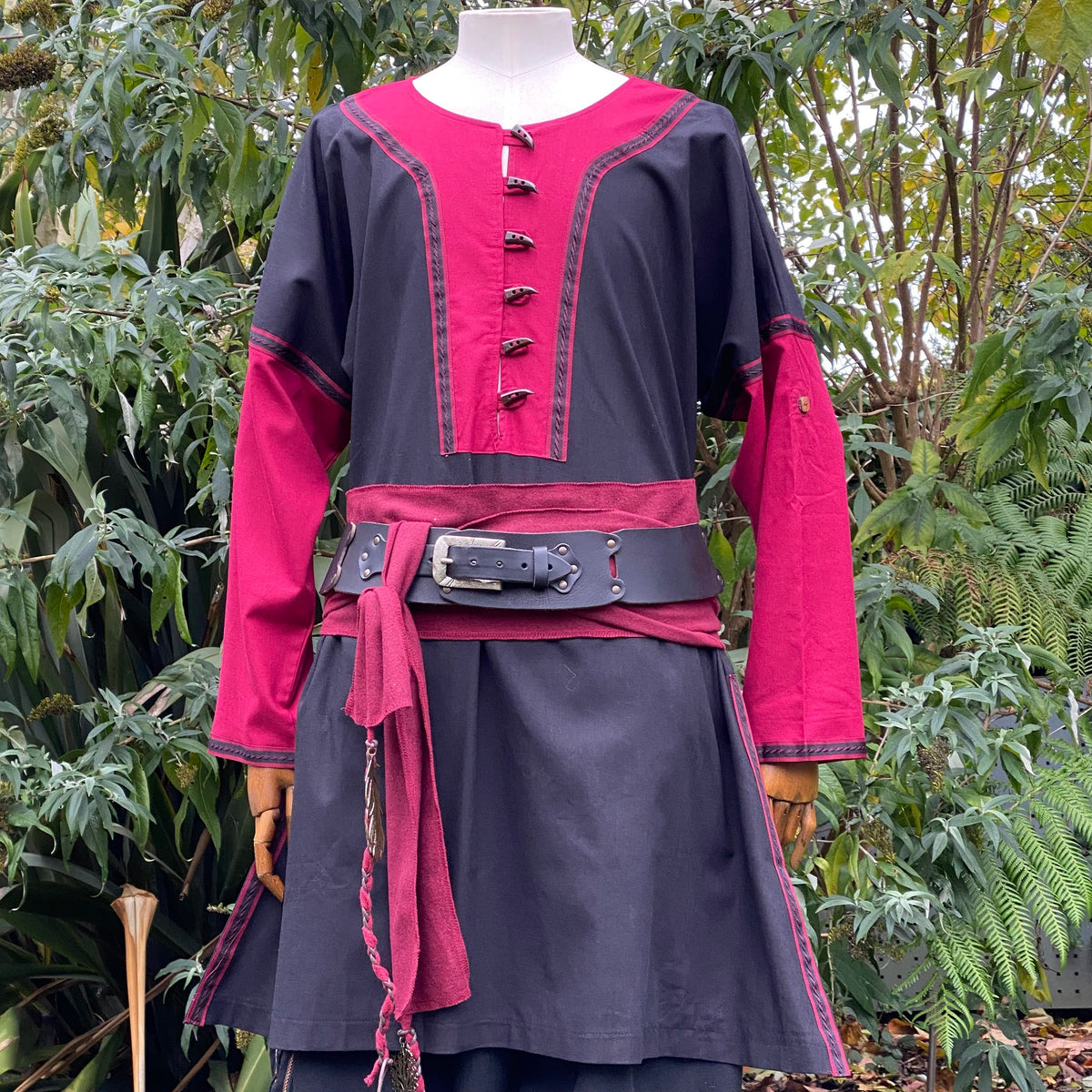 Black and red LARP tunic with ornate buttons, surrounded by greenery.