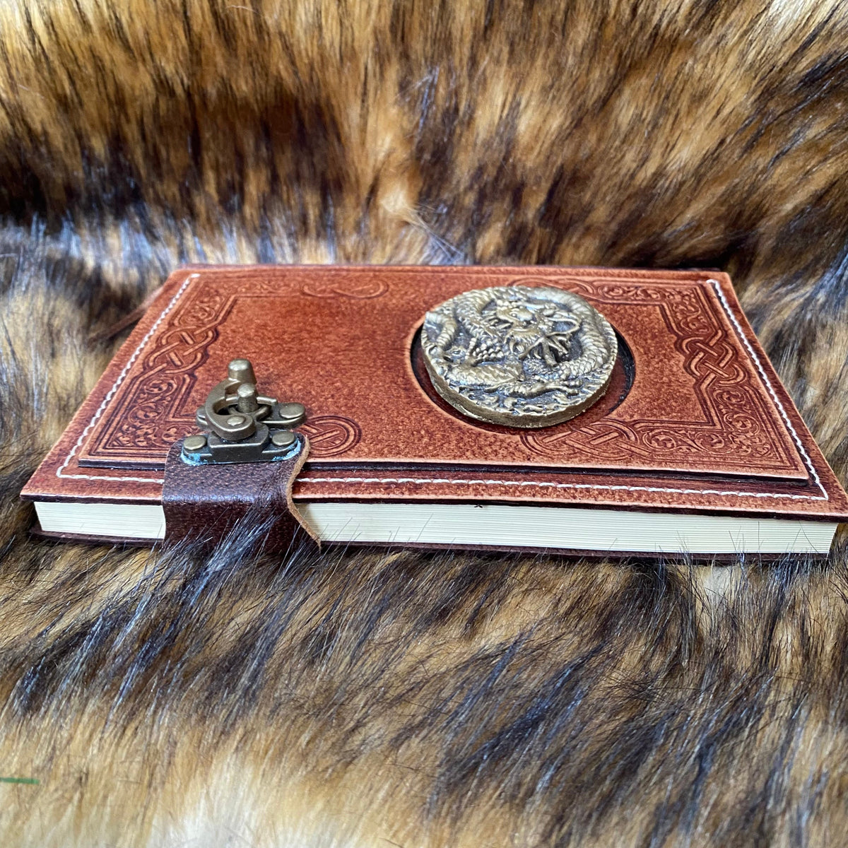 Leather LARP journal angled on fur, embossed dragon, ornate metal clasp.