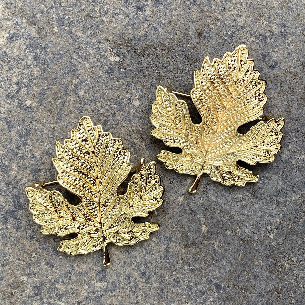 Golden elven leaf brooches on stone, textured for medieval LARP events.