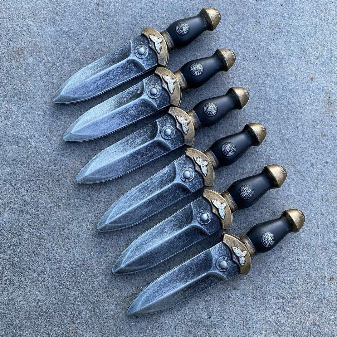 Six medieval-style LARP daggers in pewter with ornate hilts on stone.