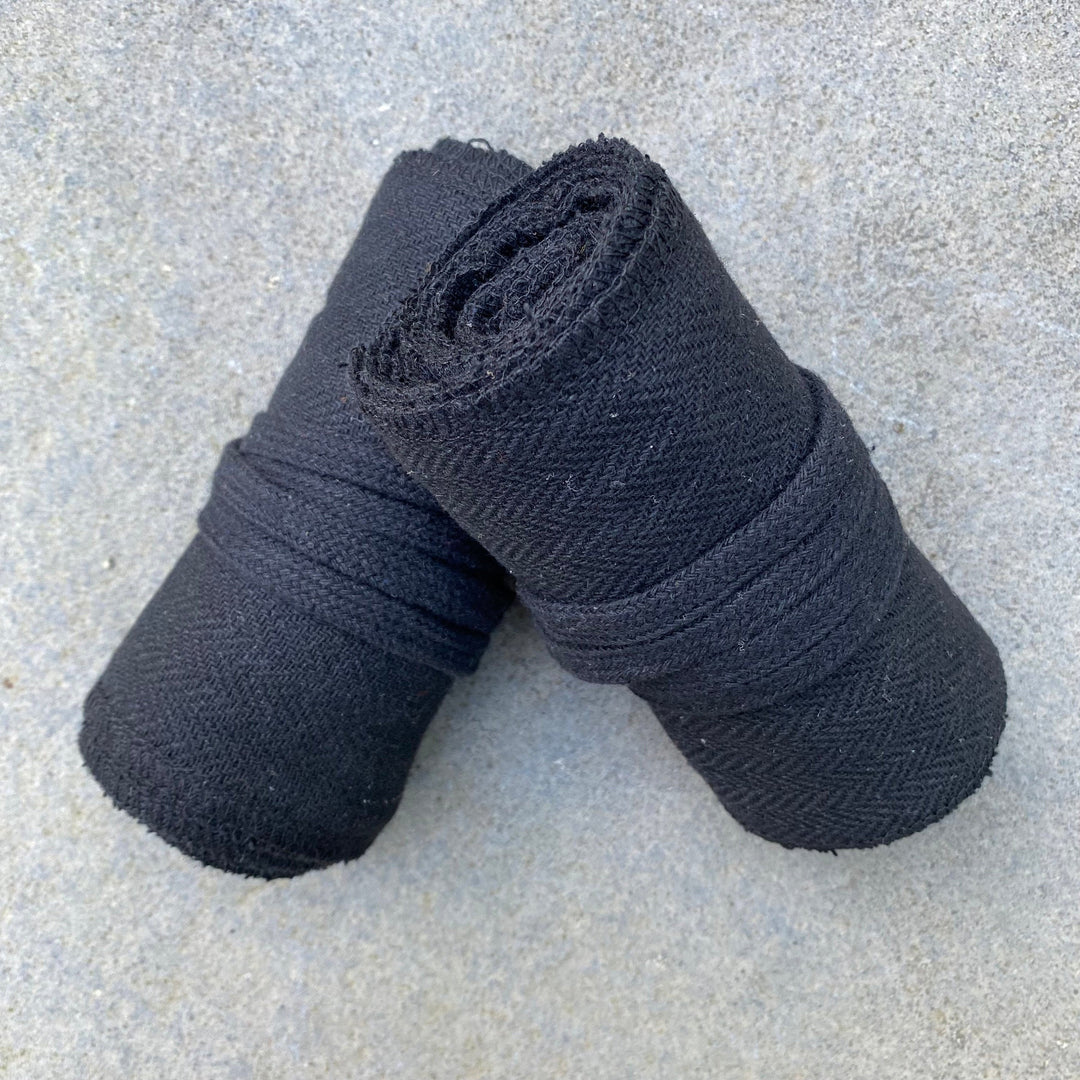 Two rolled black herringbone leg wraps on stone for LARP.