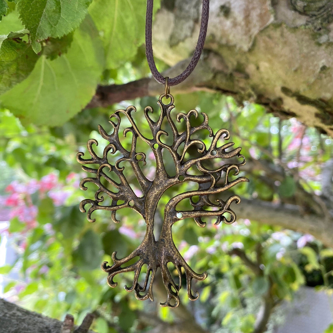 LARP medieval tree pendant in brass, hanging outdoors with lush green background.