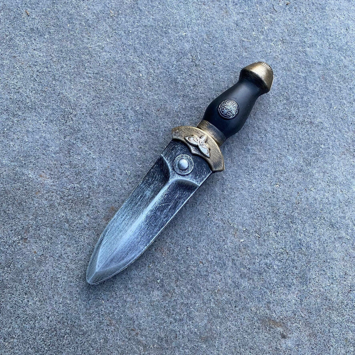 Medieval LARP foam dagger with ornate hilt, side view on a stone surface.