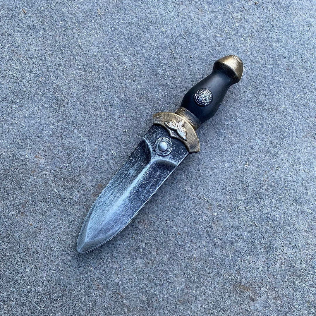 Medieval LARP foam dagger with ornate hilt, side view on a stone surface.