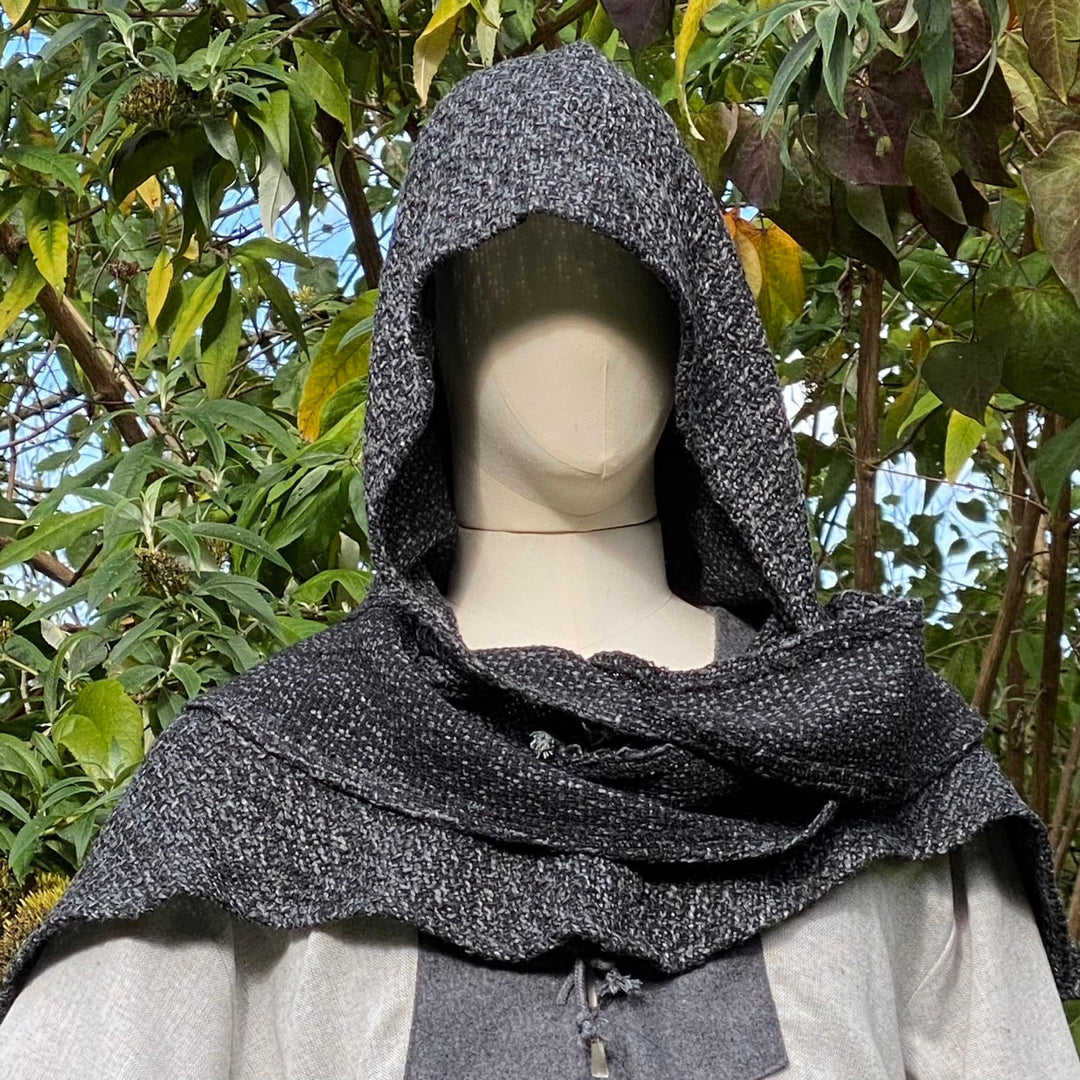 Mannequin wearing medieval LARP hood and cloak, outdoors with greenery background.